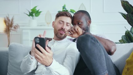 Handsome couple of romantic diverse bearded guys embracing and browsing smartphone app social media communication device staying home. LGBT family. - Powered by Adobe