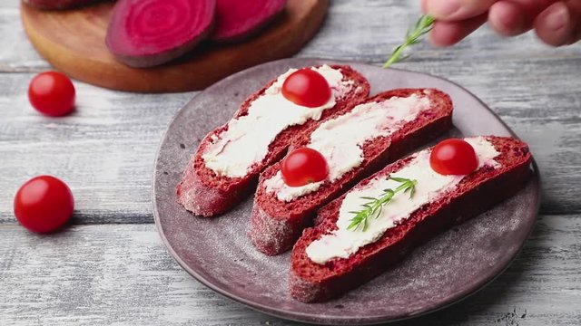 Red beet bread sandwiches with cream cheese and tomatoes decorating with herbs. Side view, close up.