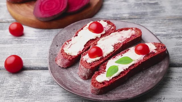 Red beet bread sandwiches with cream cheese and tomatoes decorating with herbs. Side view, close up.