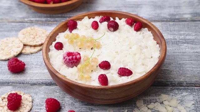 Decorating of rice flakes porridge with milk and strawberry in wooden bowl on gray wooden background. Side view, close up.