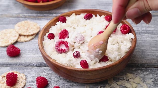 Rice flakes porridge with milk and strawberry in wooden bowl stir with a spoon on gray wooden background. Side view, close up.