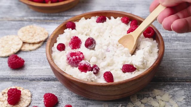 Rice flakes porridge with milk and strawberry in wooden bowl stir with a spoon on gray wooden background. Side view, close up.
