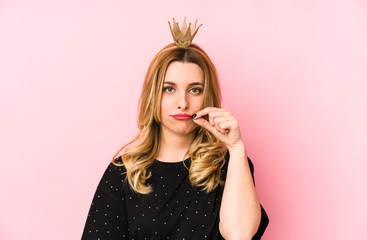 Young blonde woman wearing a crown isolated with fingers on lips keeping a secret.