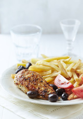 Fried chicken breast with french fries, tomatoes and olives. White wooden background. Close up.	
