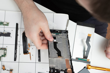 Installation of original spare parts on a mobile phone. The master repairs the smartphone on the background of disassembled parts