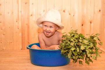 A child with a broom is sitting in a tub at the site. Traditional Russian bath. Funny hat, wellness...