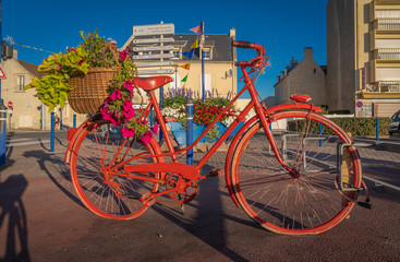 Fototapeta na wymiar Langrune Sur Mer, France - 08 04 2020: The red bicycle with its basket of flowers at sunrise