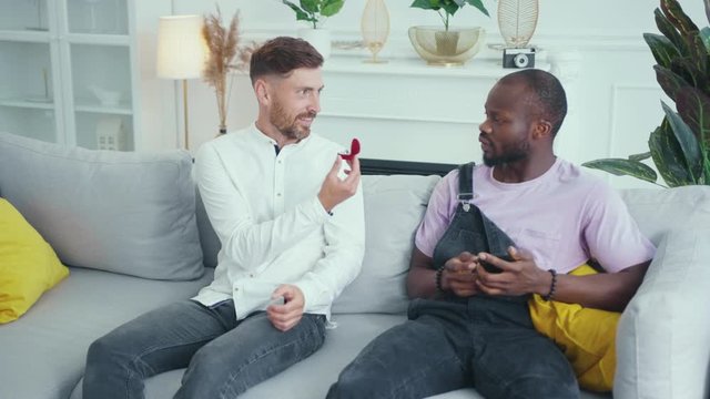 Excited caucasian gay man making marriage proposal to his best friend. Shocked and baffled african man throwing a wedding ring and walking away very angry.