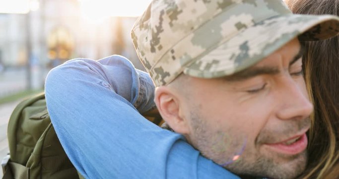 Close up of young happy Caucasian couple in love meeting and hugging outdoors at street. Handsome man soldier coming back and embracing girlfriend. Militarian guy returning from army to girl. Rear.