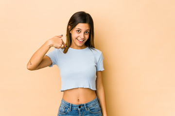 Young woman isolated on beige background person pointing by hand to a shirt copy space, proud and confident