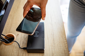 Fototapeta na wymiar Woman placing smart phone on wireless charger. Caucasian woman wirelessly charging a mobile phone. Woman putting her smartphone on wireless charger Wireless Charging Port