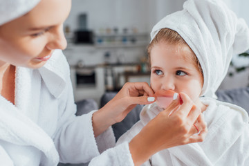 selective focus of woman applying lips patch on daughter with white towel on head