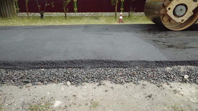 Construction of a new road. The roller levels and compacts the asphalt. Construction machinery makes a road in a small town, village. Industrialization, city development. Road surface repair