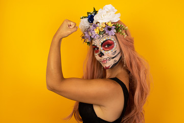 Portrait of beautiful Caucasian woman sugar skull make up isolated over yellow background,  showing...