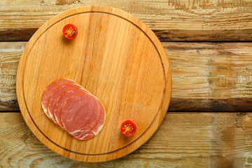 Sliced ham on a wooden board and cherry on the table.