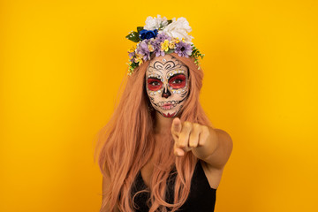 Indoor shot of cheerful young woman halloween make up indicates happily at you, chooses to compete, has positive expression. beautiful clever student makes choice, isolated on gray Wall