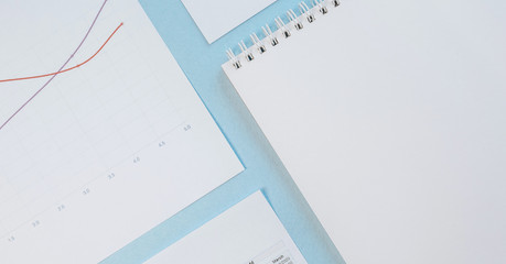 Office concept. Workspace with graphs, notebook and pencil. Copy space white and blue background.