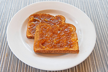 Two slices of toasted and buttered whole wheat bread on a plate with marmalade spread.