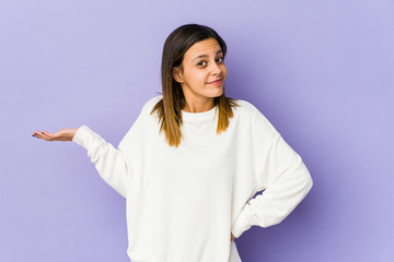 Young woman isolated on purple background doubting and shrugging shoulders in questioning gesture.