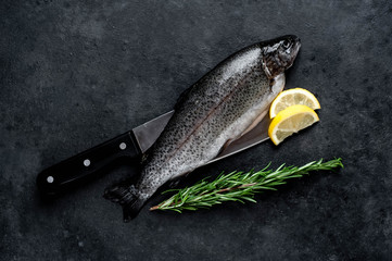 Raw fish trout with spices and ingredients on a knife on a stone background