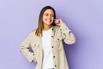 Young woman isolated on purple background covering ears with hands.