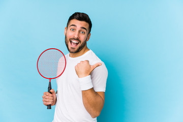 Young handsome man playing badminton isolated points with thumb finger away, laughing and carefree.