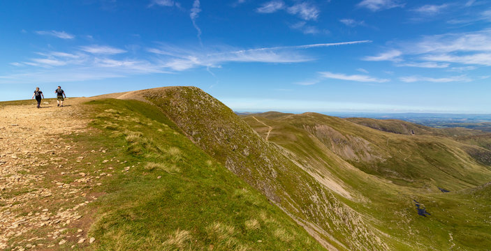 Couple of young man and woman walking over the Helvellyn peak, Lake District, Cumbria, England