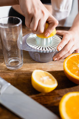 cropped view of young woman squeezing half of orange in juicer
