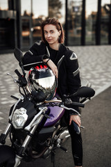 Fototapeta na wymiar Smiling girl in a motorcycle jacket sits with a motorcycle helmet on a motorbike