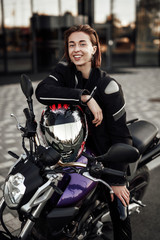 Fototapeta na wymiar Happy girl in a motorcycle jacket sits with a motorcycle helmet on a motorbike