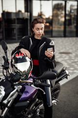 Fototapeta na wymiar Pretty girl in a motorcycle jacket sits on a purple motorbike and looks at her phone