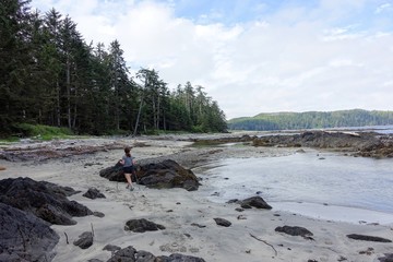 A female hiker walking along the ocean of the sandy beaches of nels bight and experimental bight, beside forest and the pacific ocean, along the beautiful cape scott trail on Northern Vancouver island
