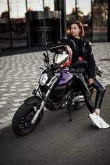 Fototapeta na wymiar Sexy girl in a black jacket sits on a purple motorbike with a red safety helmet