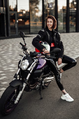 Fototapeta na wymiar Super pretty girl in a black jacket sits on a purple motorbike with a red safety helmet