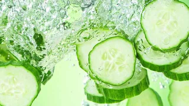 Super Slow Motion Shot of Cucumber Slices Falling into Water on Green Background at 1000fps.
