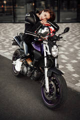 Fototapeta na wymiar Cute looking girl in a black jacket sits on a purple motorbike with a red safety helmet