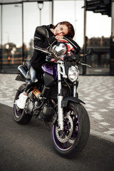 Fototapeta na wymiar Pretty lady in a black jacket sits on a purple motorbike with a red safety helmet