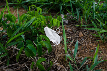 white disposable mask thrown as garbage in the middle of green plants