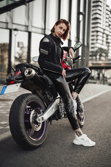 Fototapeta na wymiar Hot looking girl in a black jacket sits on a purple motorbike with a red safety helmet