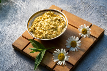 Mustard powder in saucers with mint leaves and daisies on a wooden stand on a gray background. Seasoning for dishes