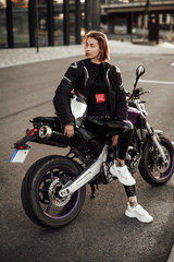 Fototapeta na wymiar Very beautiful young brunette girl in a black motorcycle jacket sits on a purple sport motorbike