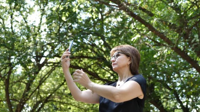 Beautiful woman, girl takes a selfie with a mobile phone, enjoying herself and rest in the park.slow motion
