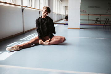Happy ballet dancer stretching legs on floor in studio
