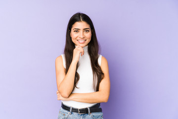 Young indian woman isolated on purple background smiling happy and confident, touching chin with...