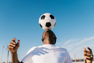 Close-up of young man balancing soccer ball on head against blue sky