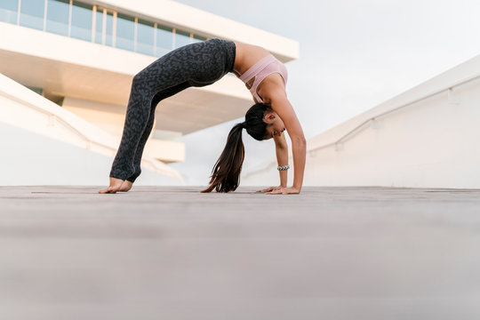 Female athlete practicing wheel pose against building in city