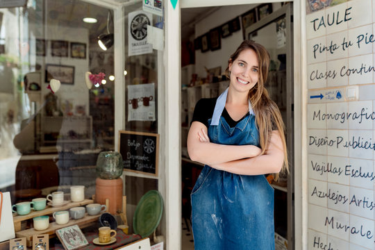 Smiling young woman with arms crossed standing at entrance of studio