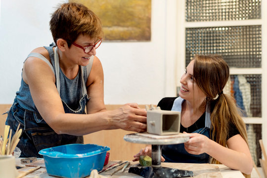 Mature woman teaching pottery to coworker in workshop
