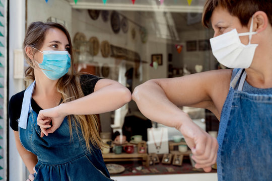 Close-up of female coworkers wearing masks giving elbow bump while standing outdoors