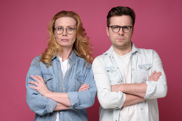 Serious business team of mature man and woman in glasses looking at camera. Studio shot on pink wall.